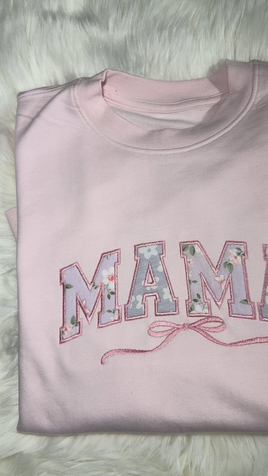 Pink 'MAMA' sweatshirt and floral baby outfit on a fluffy white surface