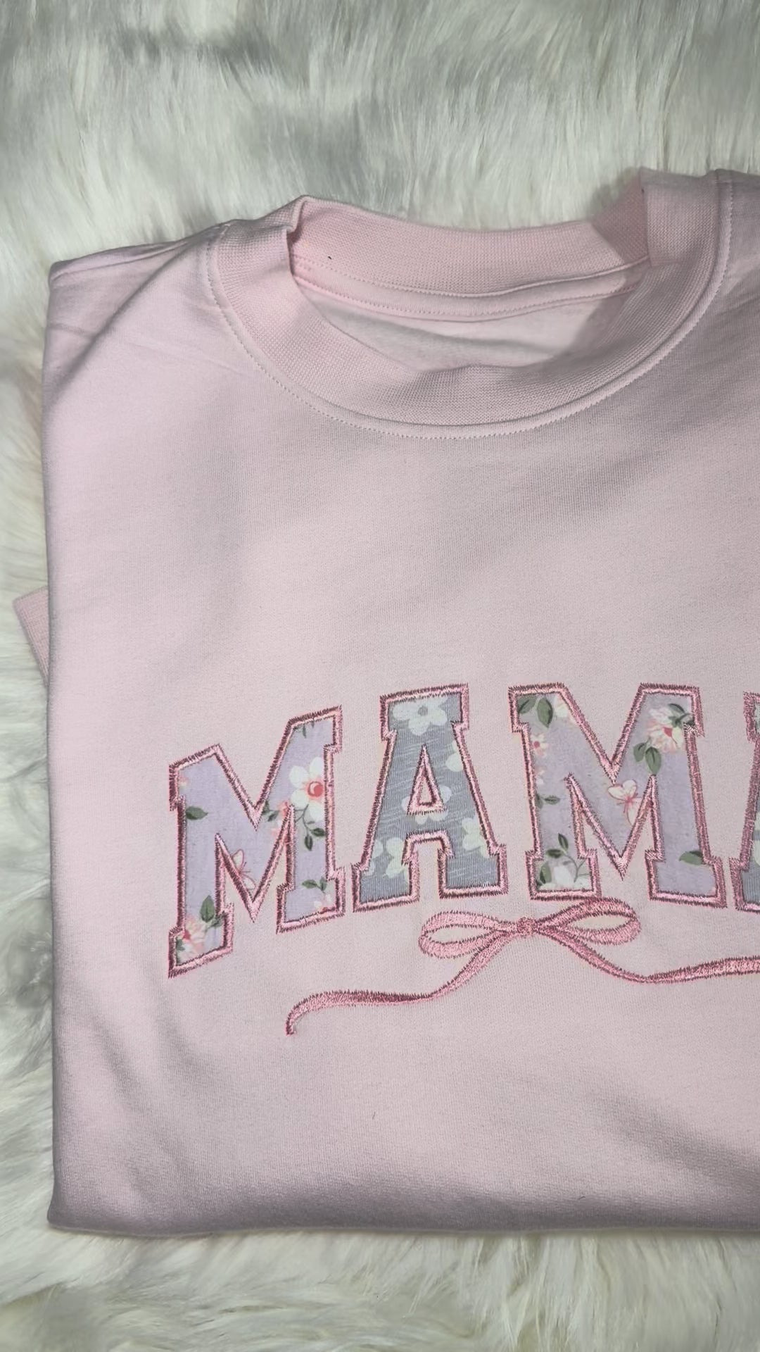Pink 'MAMA' sweatshirt and floral baby outfit on a fluffy white surface